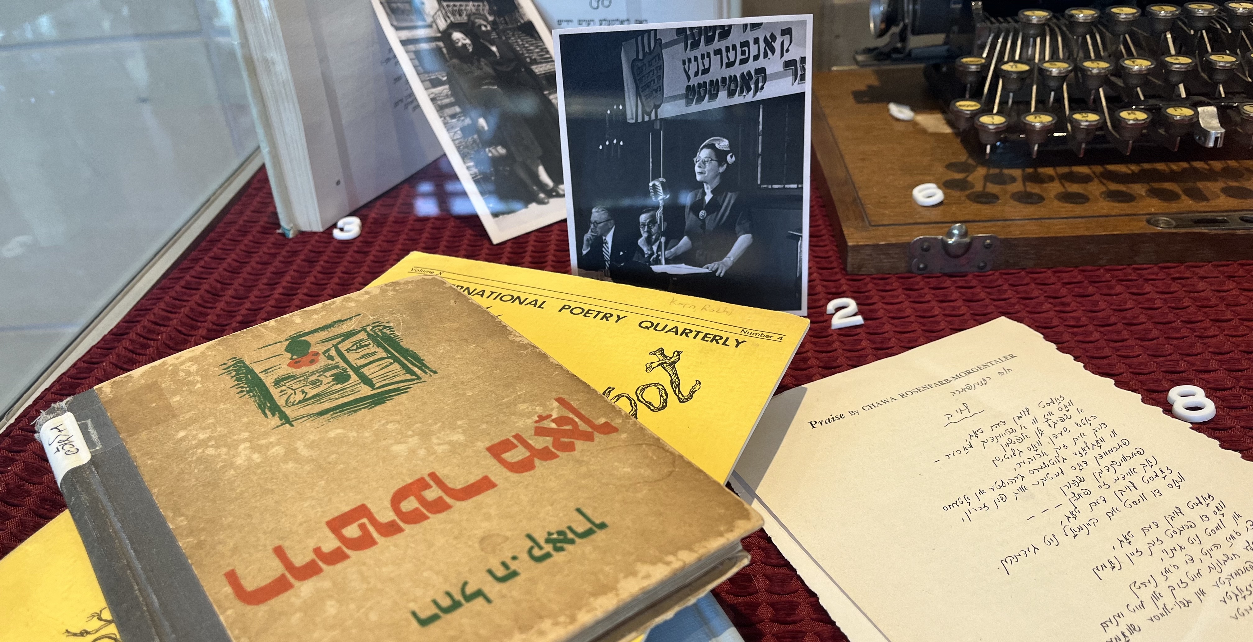 A close-up view of the exhibition case in the main lobby of our building, featuring poetry books, photographs of poets, and an antique Yiddish typewriter.